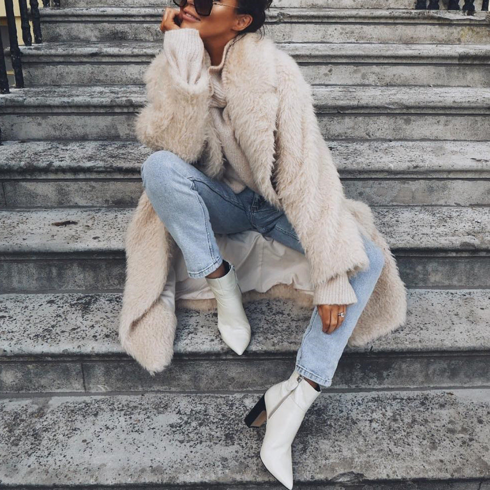 Person sitting on stone steps wearing a fluffy beige coat, light blue jeans, and white ankle boots.
