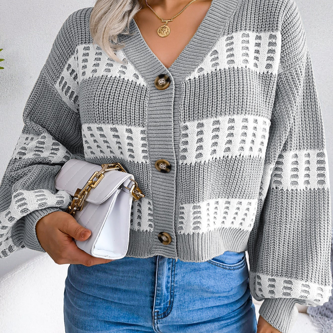 Person wearing a gray and white patterned cardigan with blue jeans on a plain background