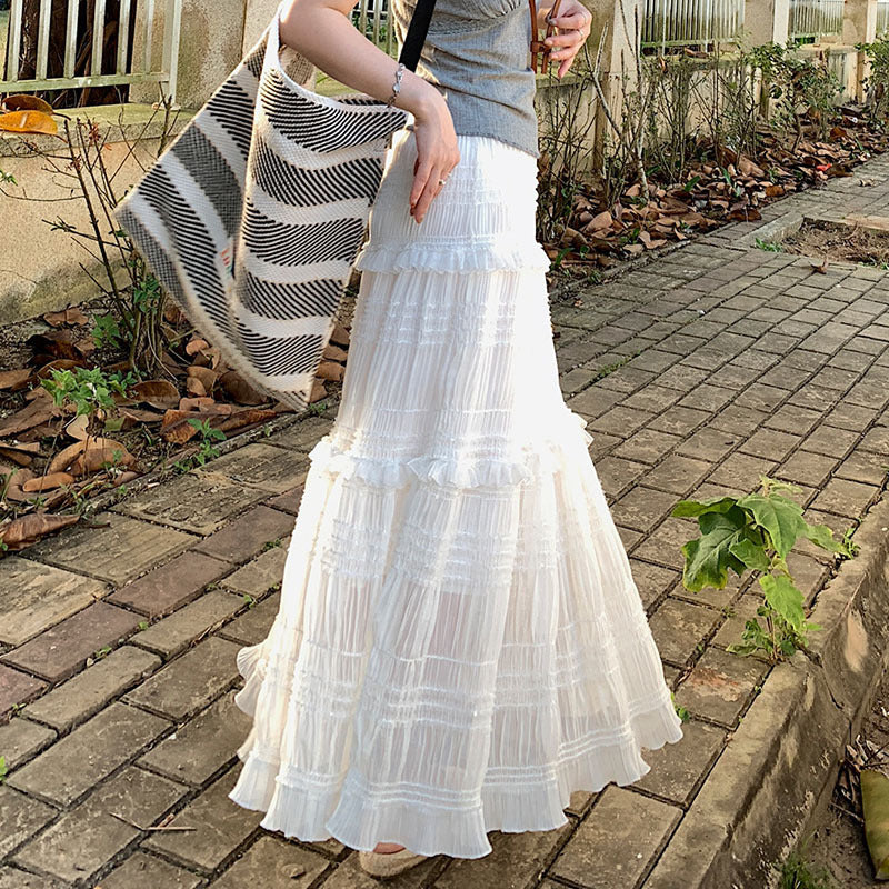 Person wearing a white tiered dress holding a striped bag on a brick path.