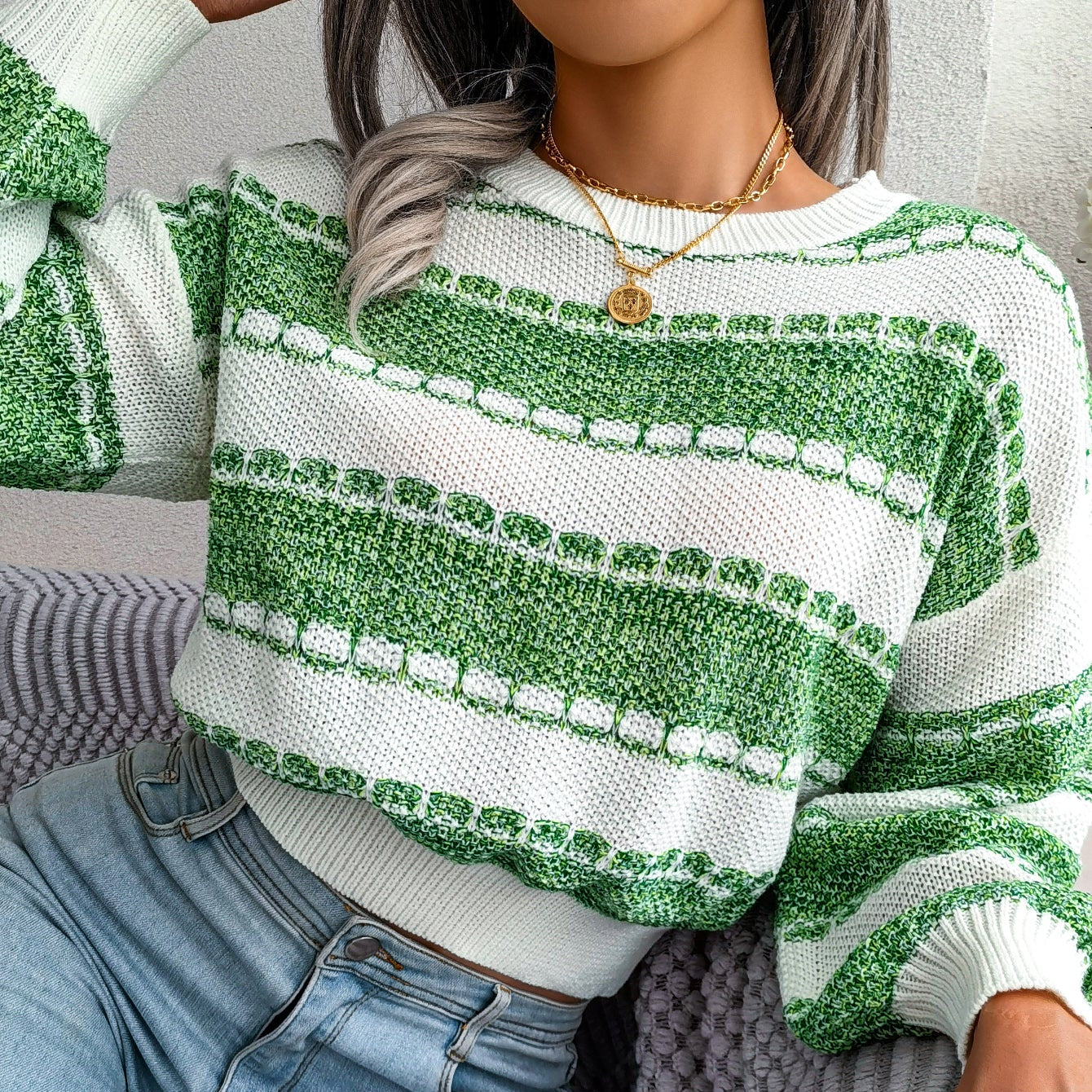 Person wearing a green and white striped sweater with light blue jeans, sitting on a gray couch.