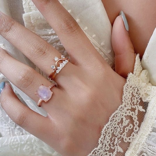 Close-up of a hand wearing two rose gold rings with gemstones on a lace fabric background.