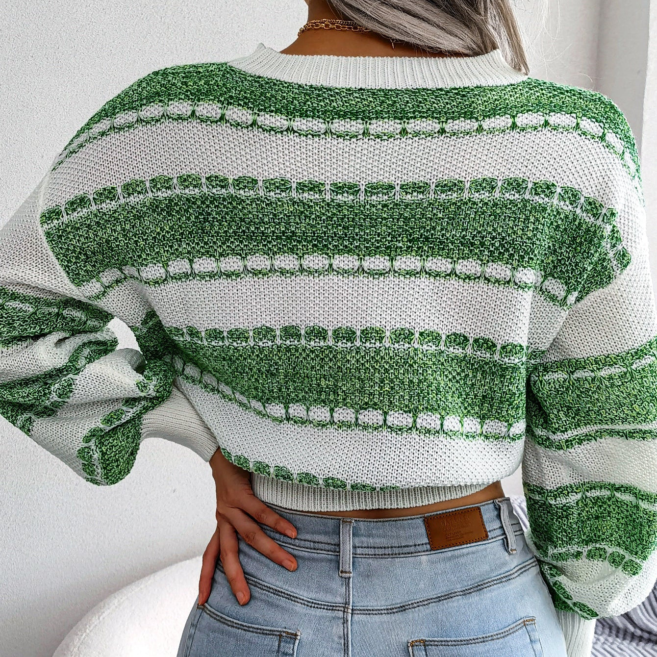Person wearing a green and white patterned sweater with blue jeans indoors.