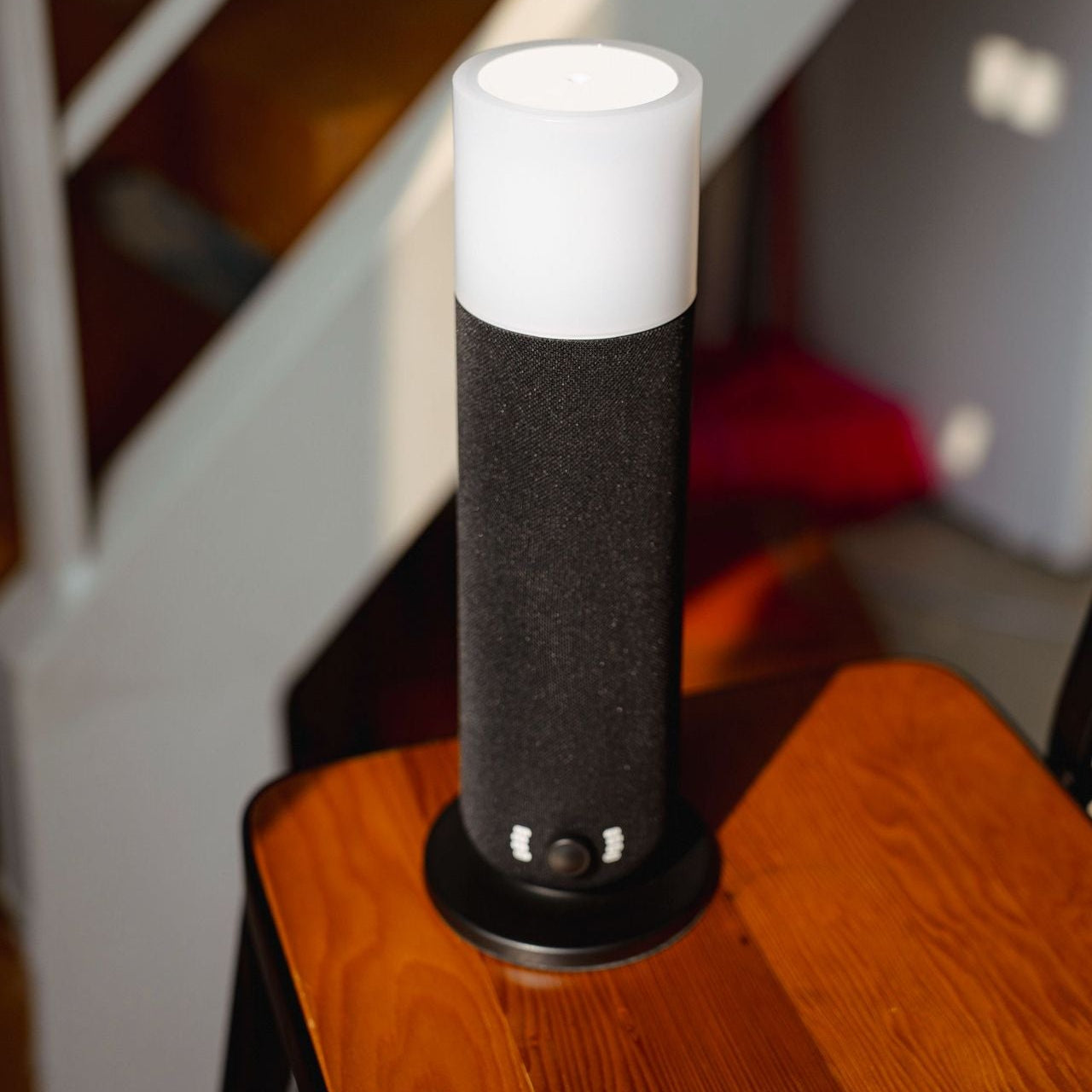 Black cylindrical device with white top on a wooden surface, staircase in the background