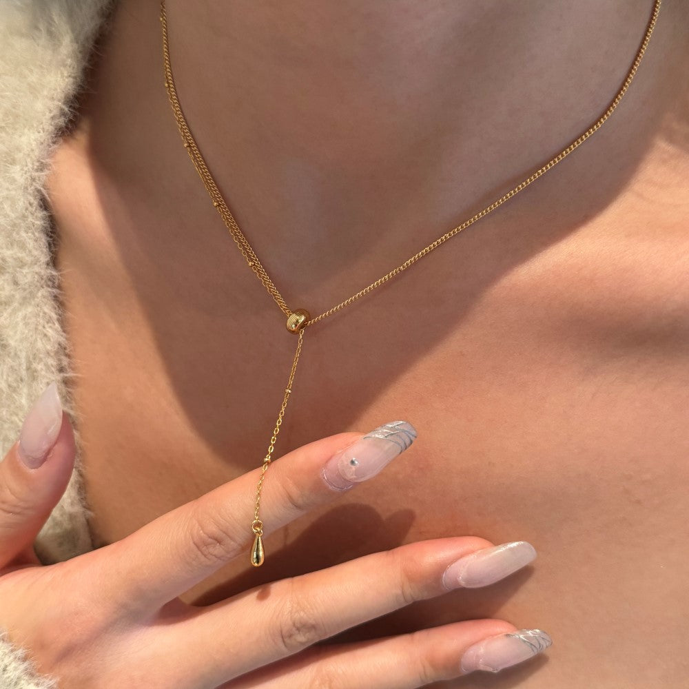 Gold necklace with a teardrop pendant worn by a person with light pink nail polish.