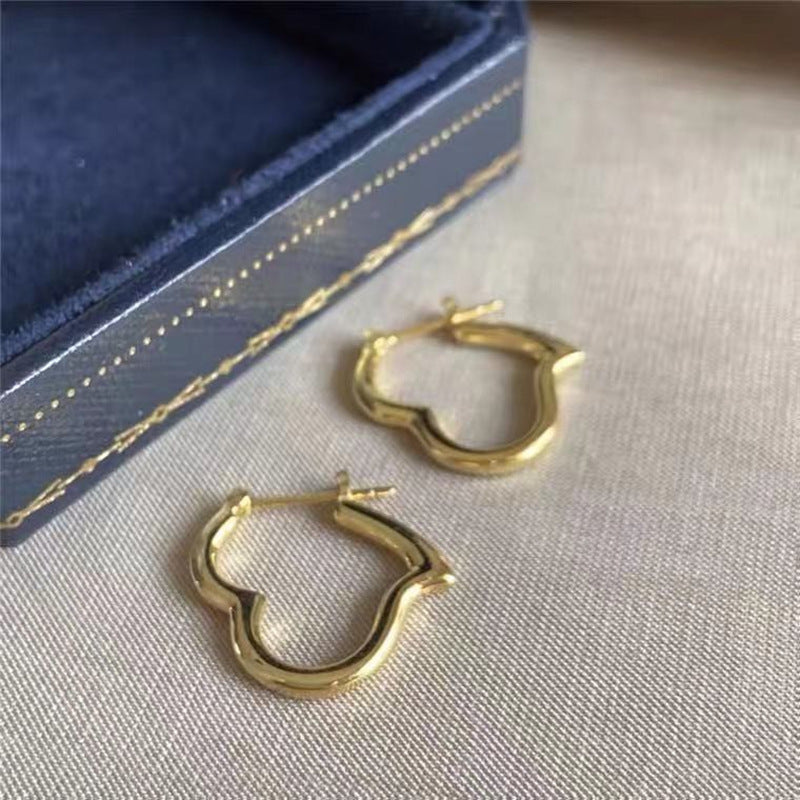 Gold heart-shaped hoop earrings on a textured surface with a blue jewelry box in the background.