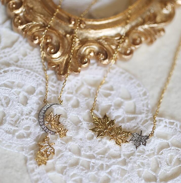 Gold necklaces with leaf and moon pendants on a white lace background
