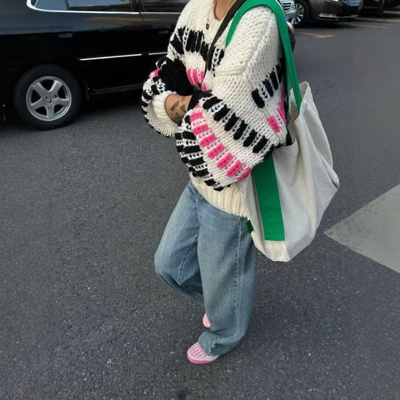 Person wearing a patterned sweater and jeans walking on a street.
