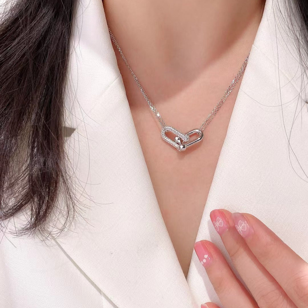 Silver heart-shaped necklace worn by a person in a white outfit.
