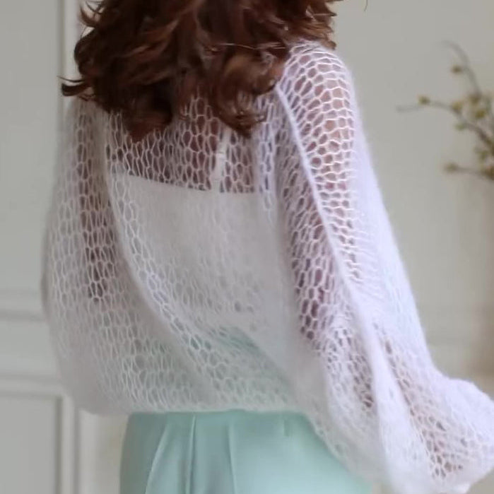 Person wearing a sheer white lace top over a light green outfit indoors.