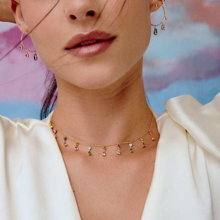 Close-up of a woman wearing a delicate necklace with colorful beads against a blurred background.