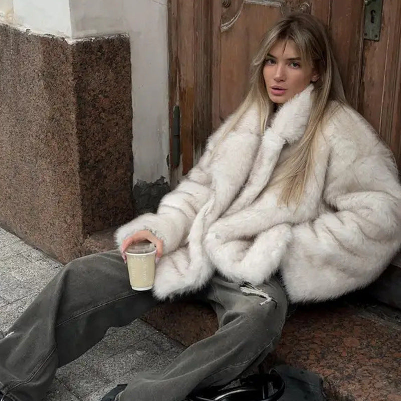 Person wearing a white fur coat sitting on the ground with a cup.