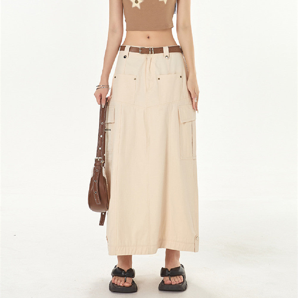 Person wearing a beige long skirt with a brown belt, holding a brown bag on a white background