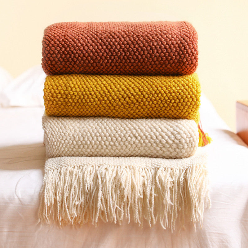 Stack of three knitted blankets in brown, yellow, and beige on a light surface.
