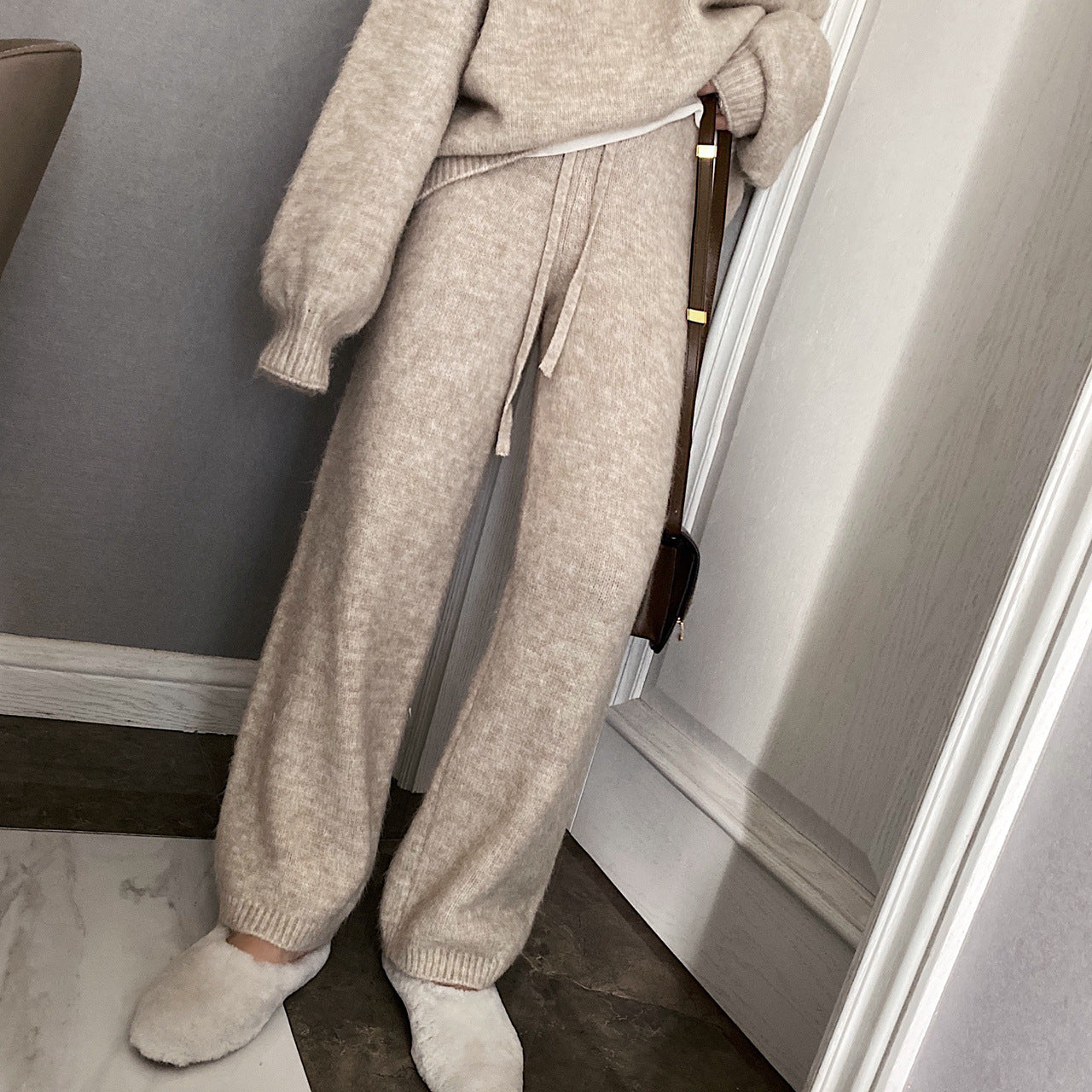 Person wearing a beige sweater and pants standing in a room with a neutral color scheme.