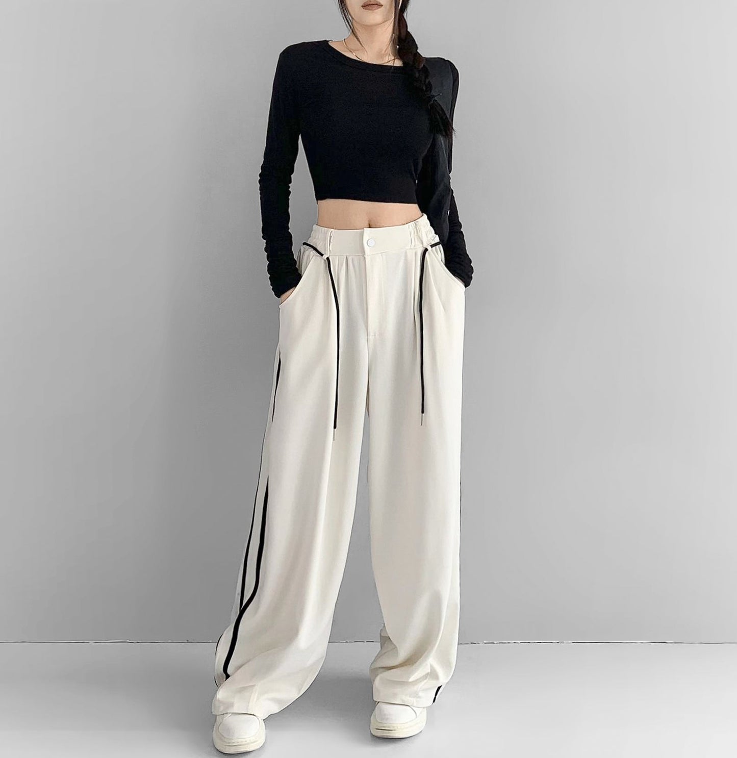 Person wearing a black long-sleeve top and white wide-leg pants on a gray background
