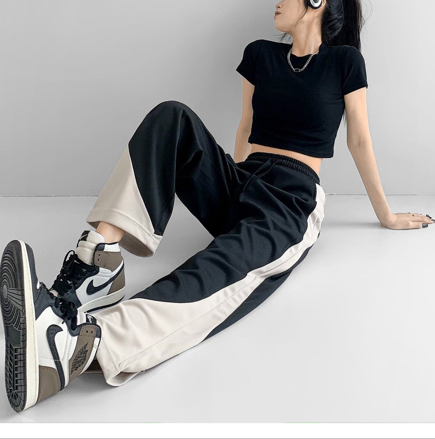 Person wearing black and white outfit with Nike shoes on a plain background