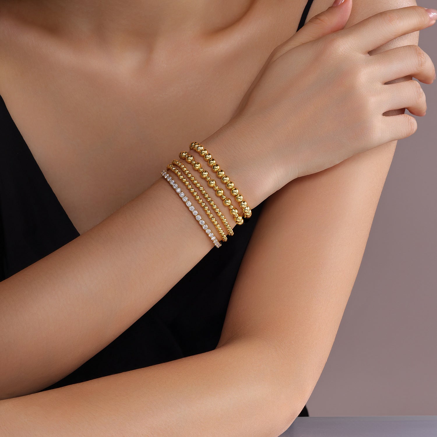 Gold bracelets on a model's wrist against a neutral background