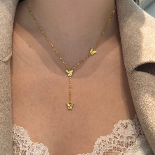 Gold butterfly necklace worn by a person with a beige coat and lace trim.