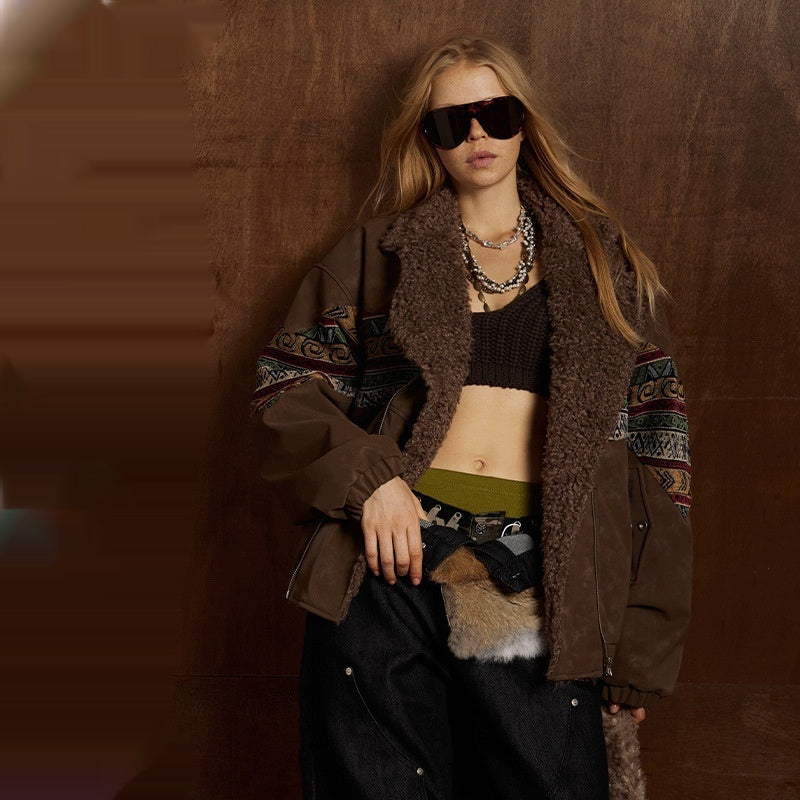 Woman wearing a brown coat with patterned sleeves, sunglasses, and a necklace against a brown background.