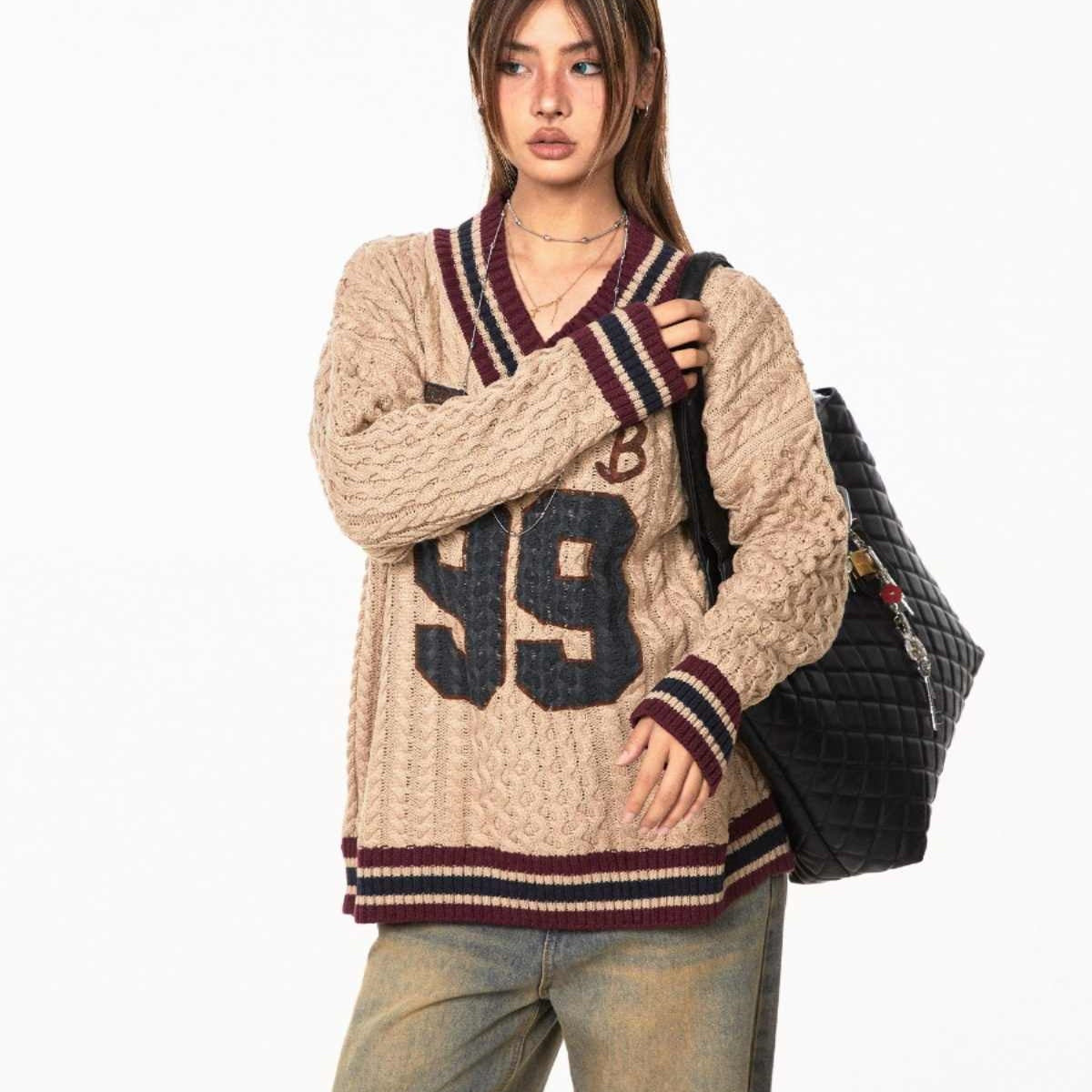 Person wearing a beige sweater with number 99 design, holding a black backpack on a white background