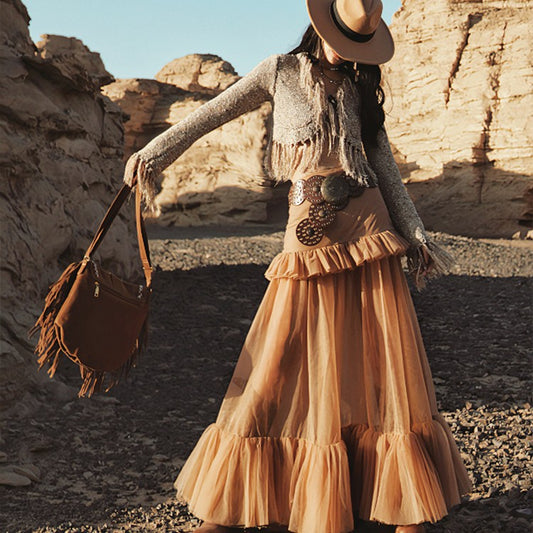 Woman in a long beige skirt and gray cardigan standing in a desert landscape.