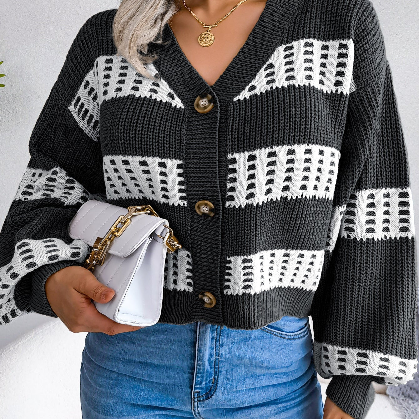 Person wearing a black and white patterned cardigan with blue jeans against a neutral background