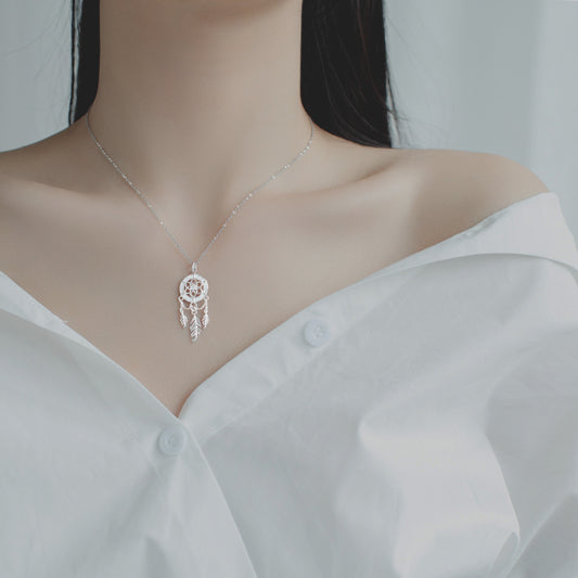 Silver necklace with a dreamcatcher pendant on a mannequin wearing a white blouse.
