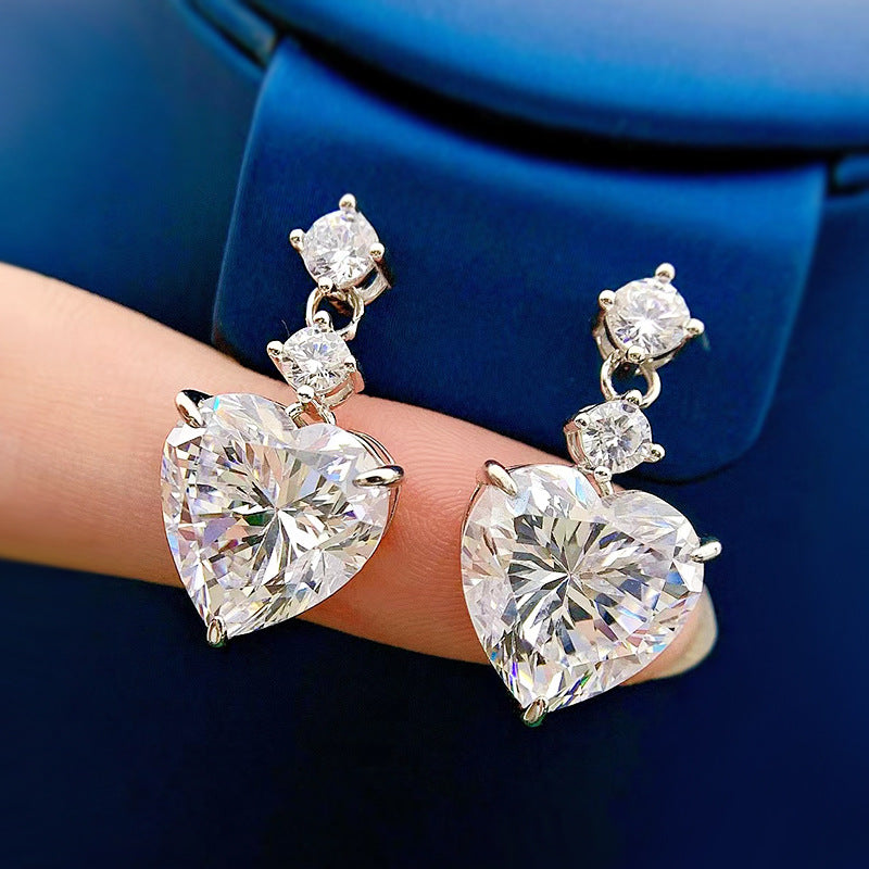 Heart-shaped diamond earrings on a hand with a blue background