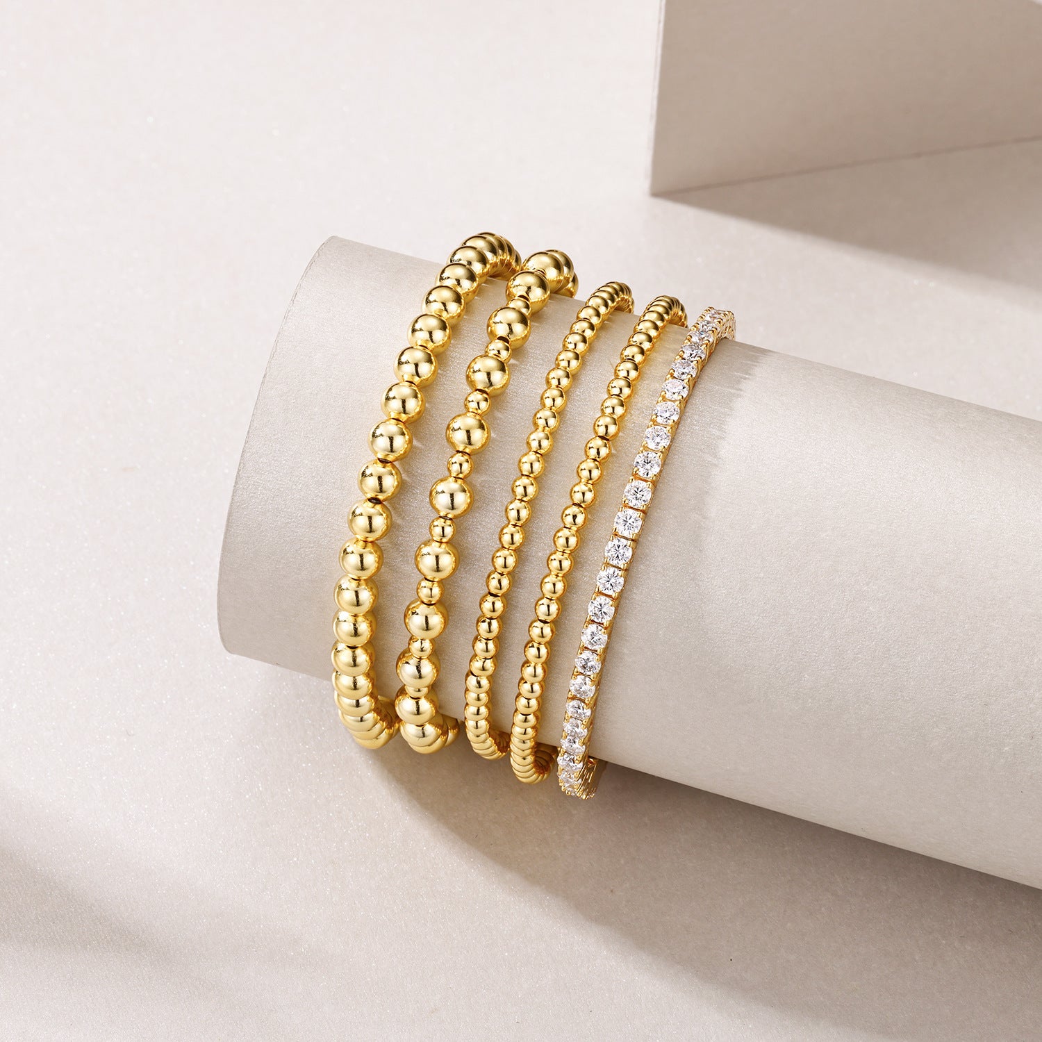Three gold bracelets with varying designs on a white cylindrical stand.
