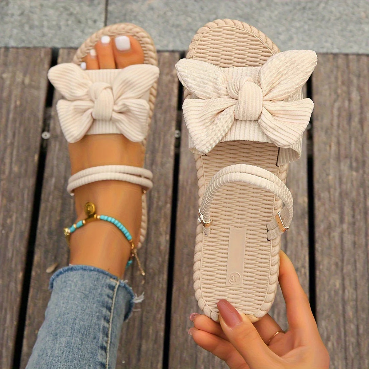 Beige sandals with large bows held by a person against a wooden background