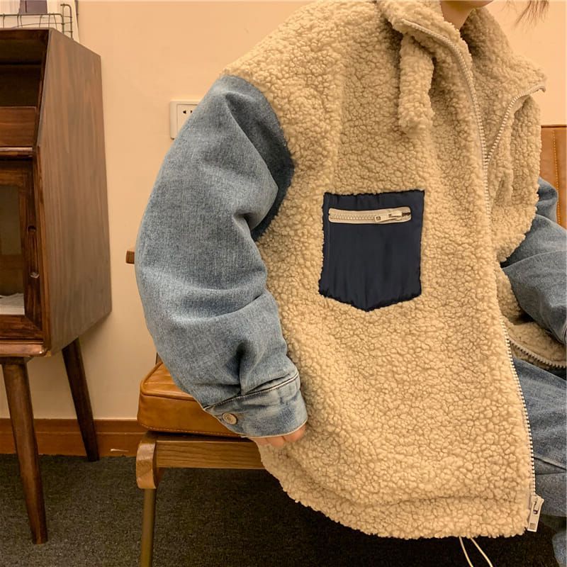 Person wearing a beige fleece vest with a blue pocket and denim sleeves indoors.