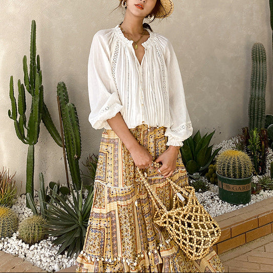 Woman in a white blouse and patterned skirt standing among cacti and succulents.
