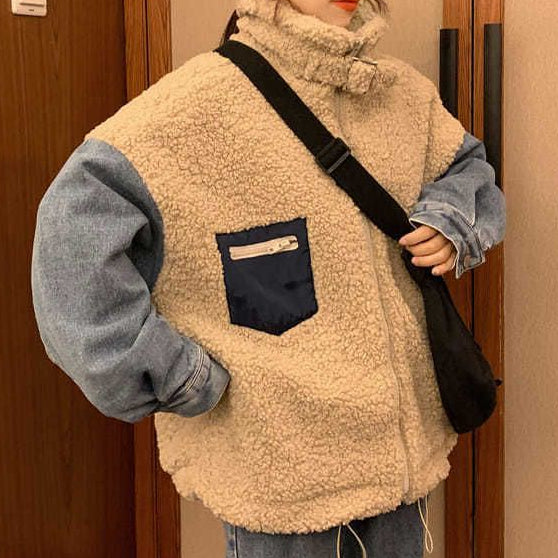 Person wearing a beige fleece vest over a blue sweater, holding a black bag indoors.