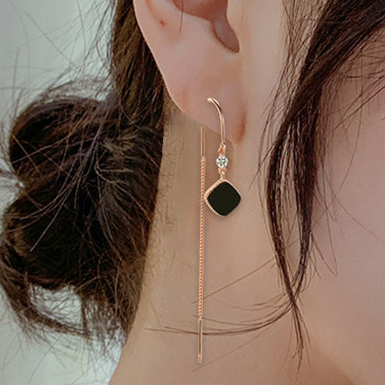Close-up of an ear wearing a gold earring with a black gemstone on a neutral background