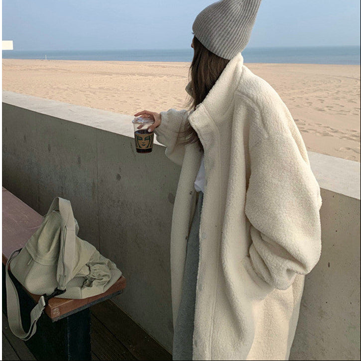 Person wearing a beige coat and knit hat by a beach.