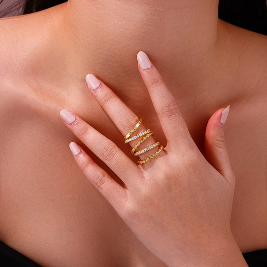 Close-up of a hand wearing multiple gold rings on a neutral background