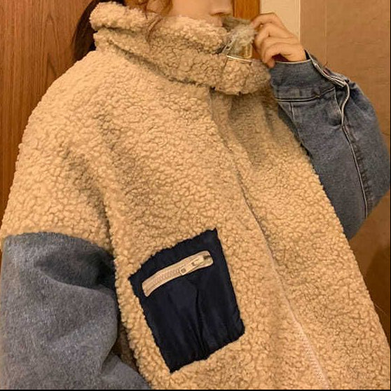 Person wearing a beige fleece jacket with blue sleeves and a black cap in a bathroom.