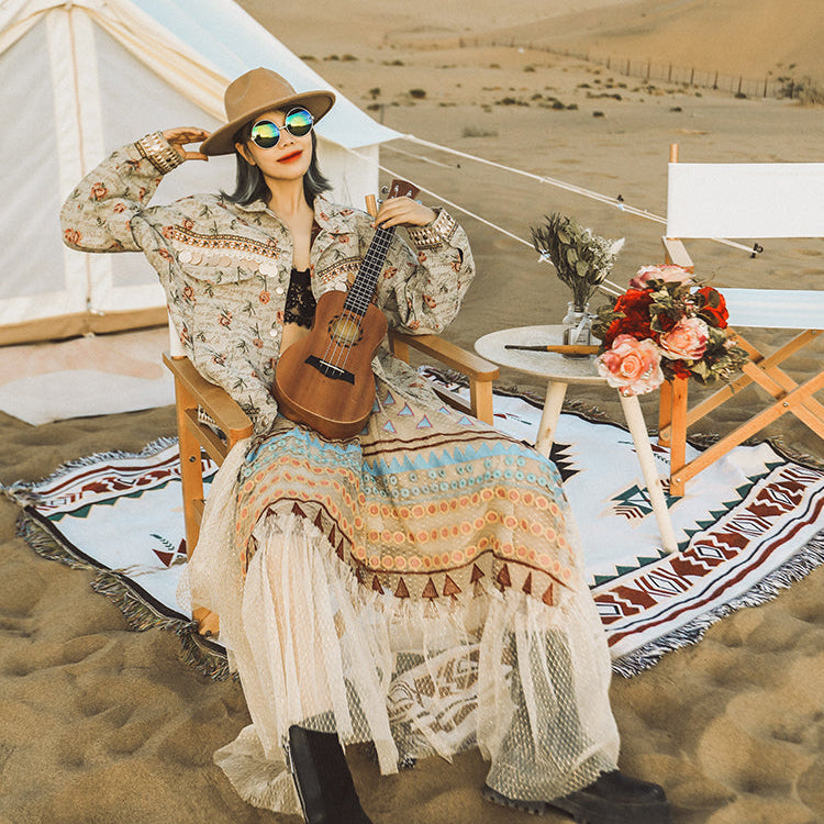 Woman in a desert setting with a tent, guitar, and flowers.