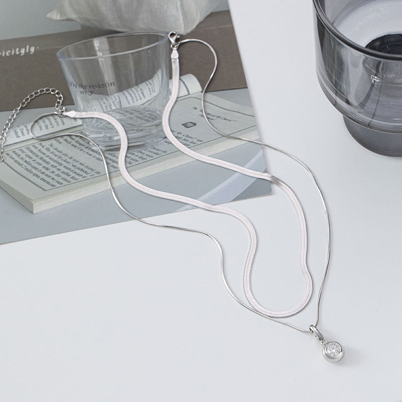 Necklace with a pendant on a light surface with a book and glass in the background