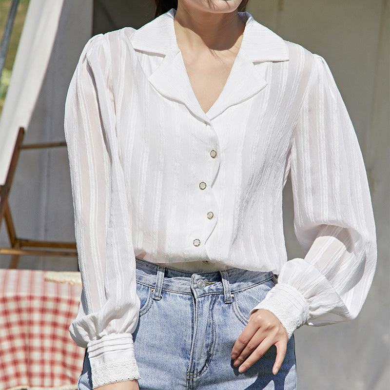 Person wearing a white blouse with puffed sleeves and blue jeans outdoors.
