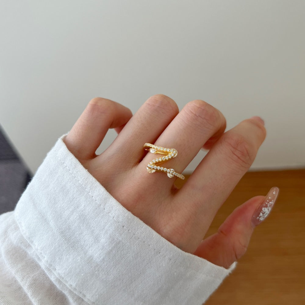 Hand wearing a gold ring with a white sleeve on a neutral background