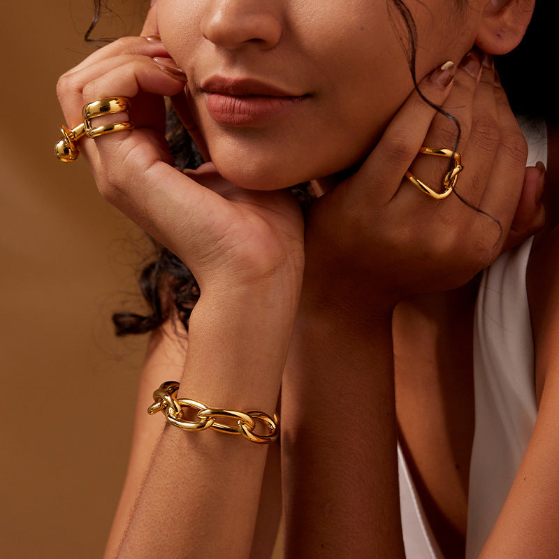 Close-up of a person wearing gold jewelry including earrings, ring, and bracelet against a brown background.