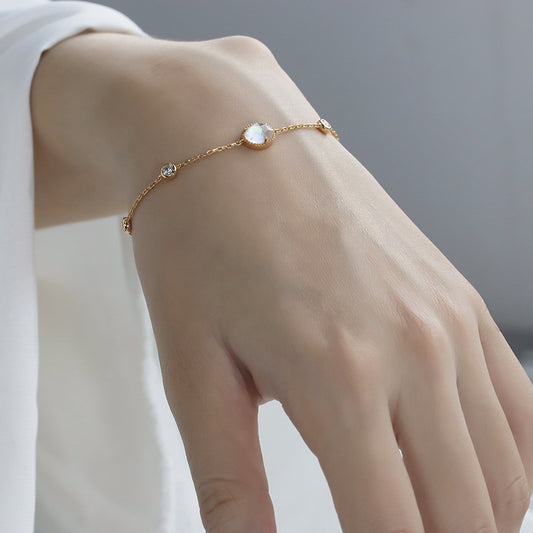 Gold bracelet with a central gemstone on a wrist against a neutral background