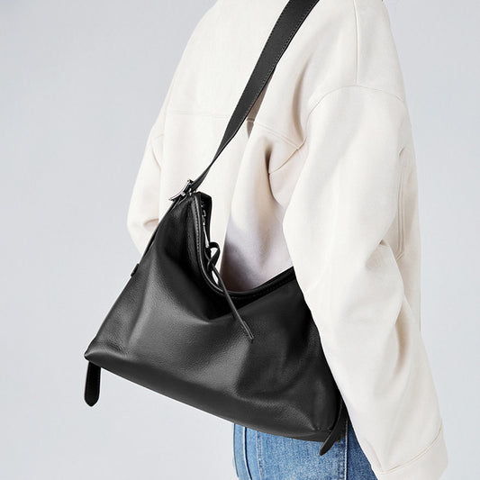 Black shoulder bag worn by a person in a white jacket and blue jeans on a light gray background