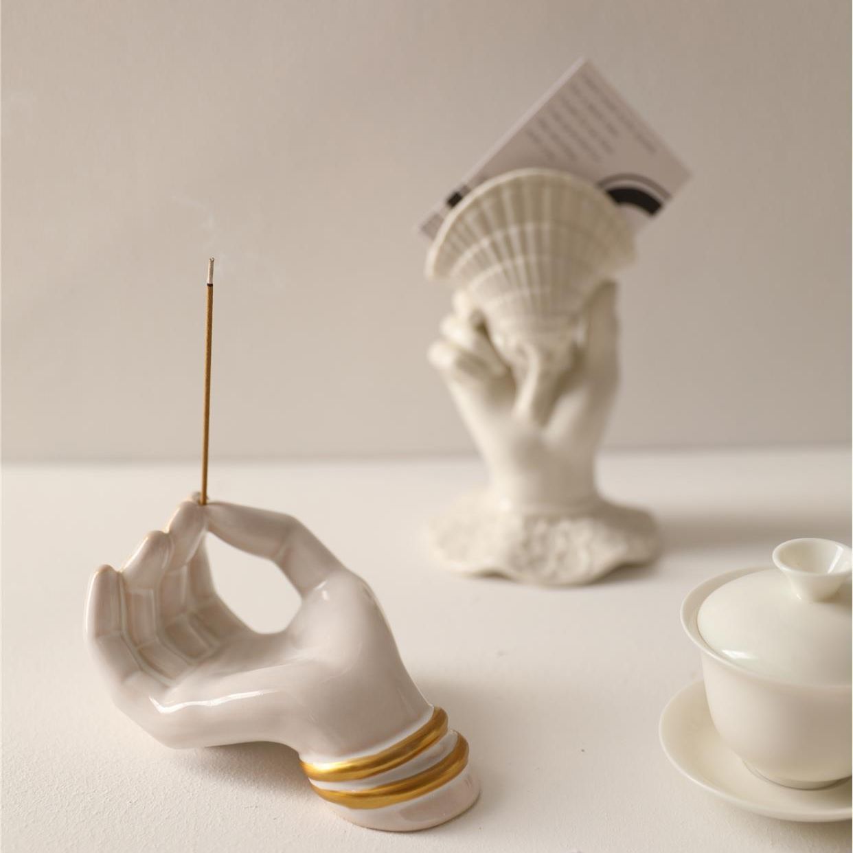 Ceramic hand holding a light bulb with an incense stick, placed on a white surface.