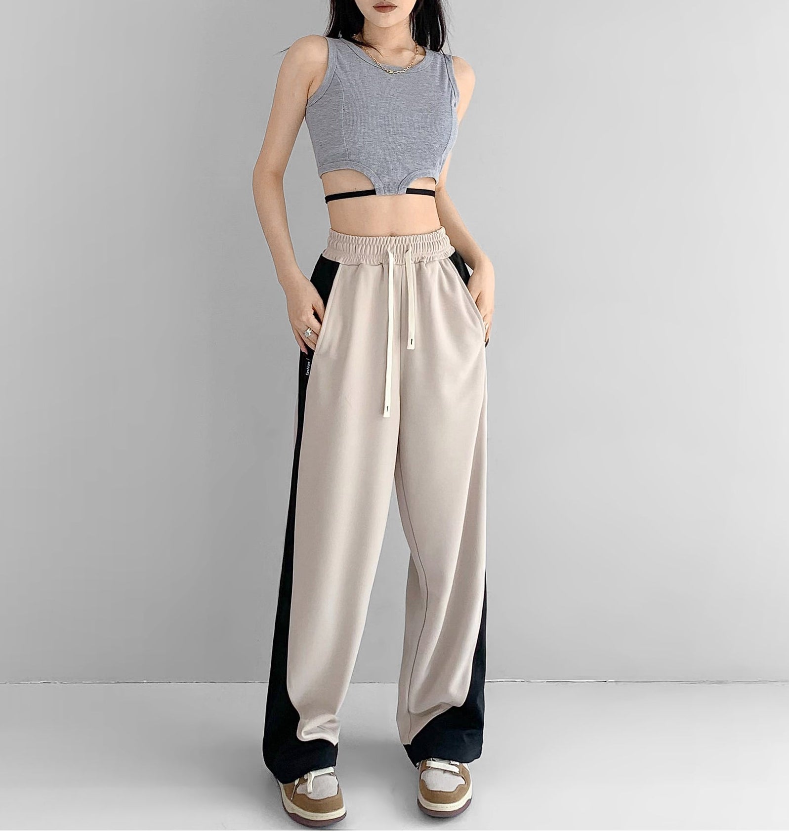 Woman wearing a gray sleeveless top and beige high-waisted pants with black sides on a plain background