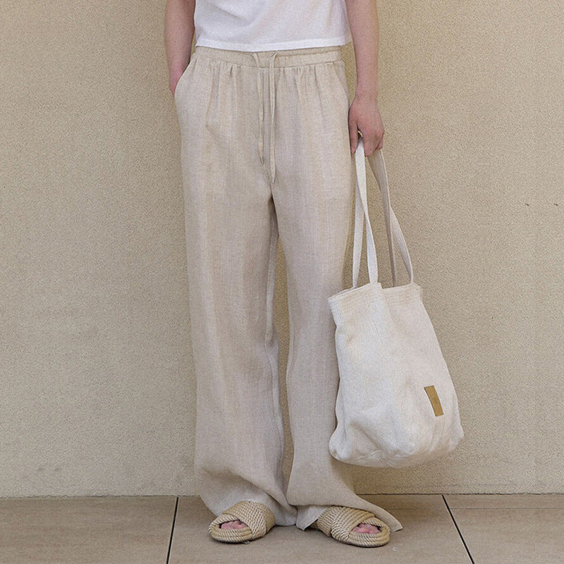 Person wearing beige wide-leg pants holding a white tote bag against a plain background