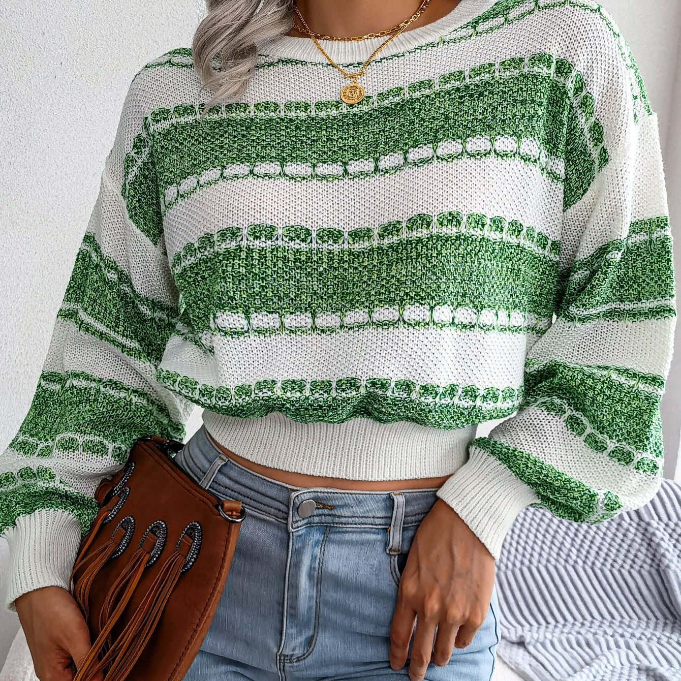 Person wearing a green and white striped sweater with blue jeans and a brown leather bag.