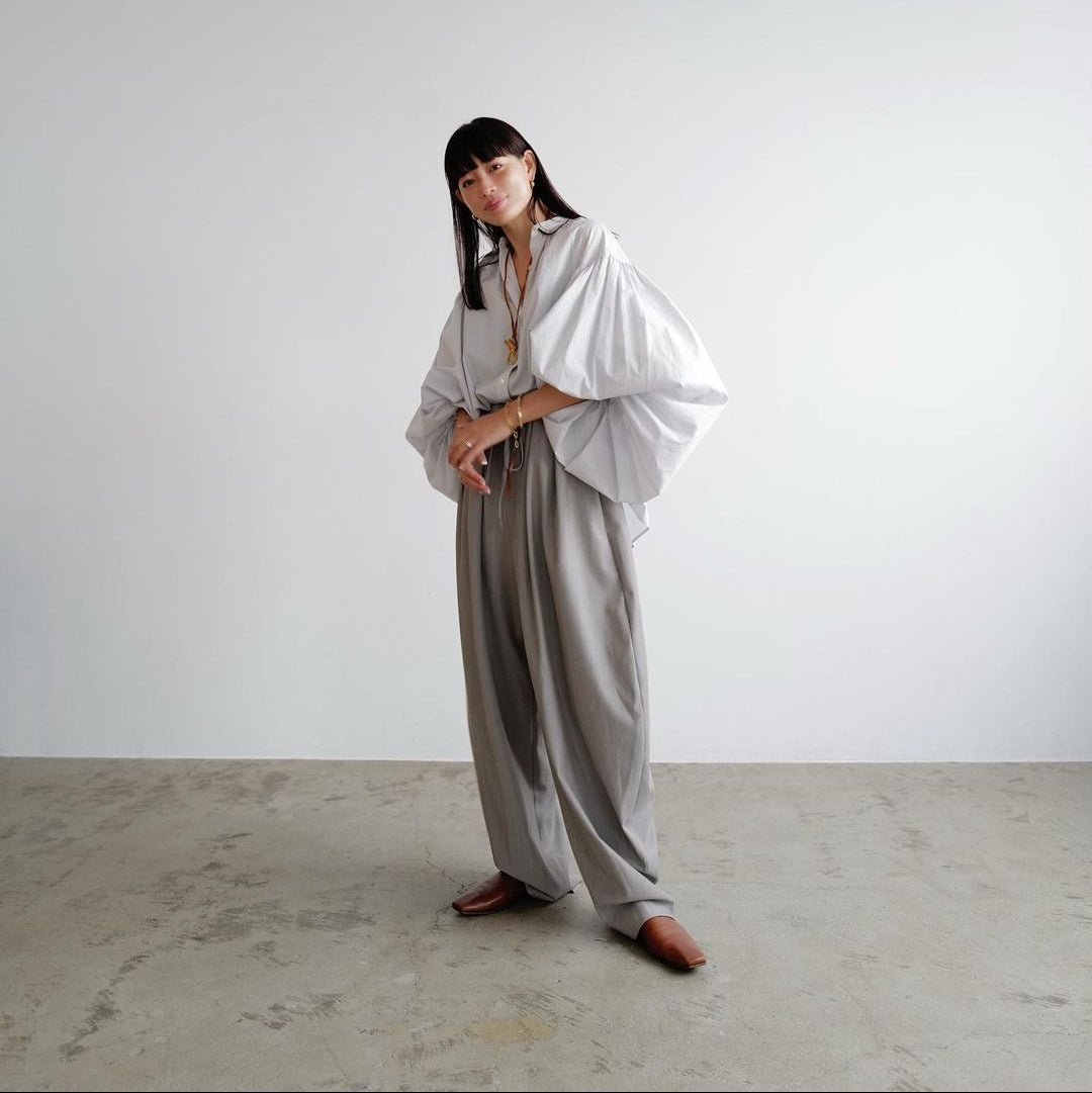 Person wearing a white blouse and gray pants against a plain background
