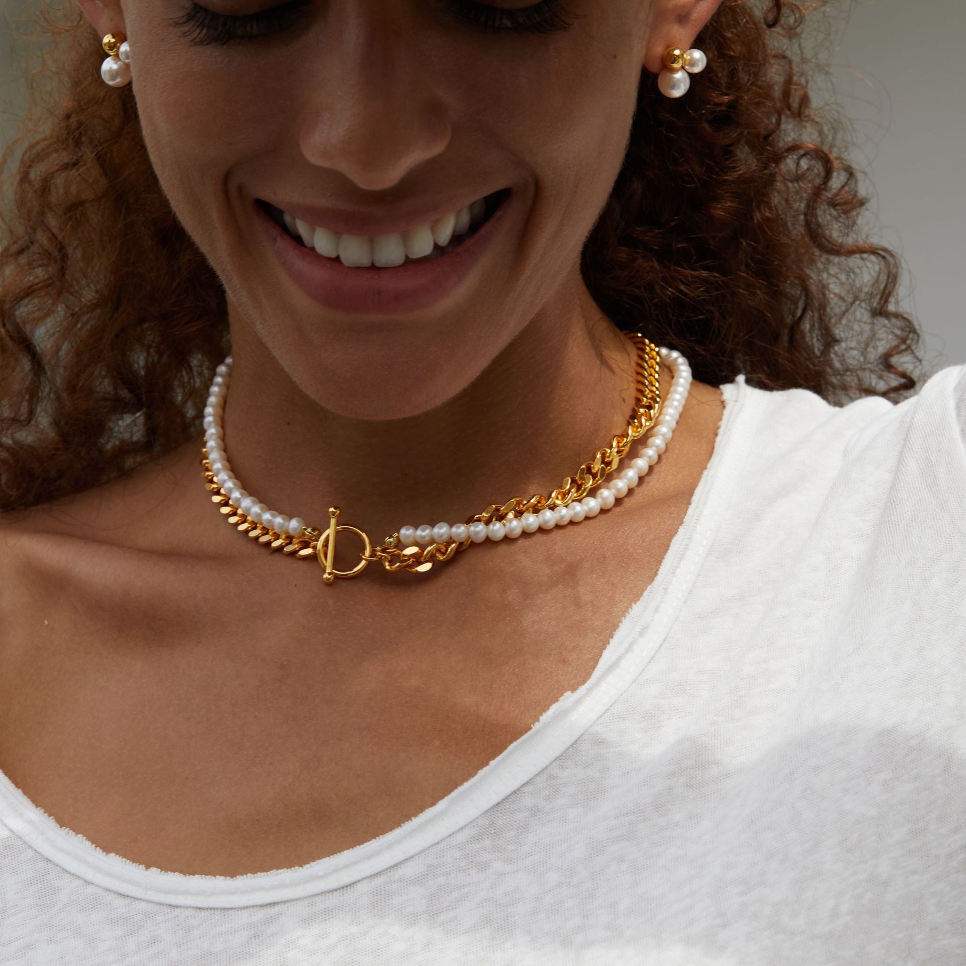 Woman wearing a gold necklace with a pearl choker and matching earrings.
